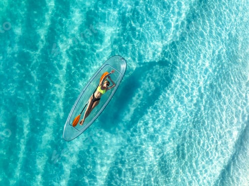 Preview: Aerial view of young woman lying on transparent canoe in blue se