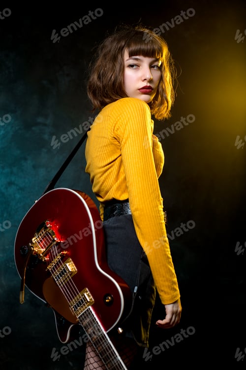 Preview: Portrait of beautiful young hipster woman with curly hair with red guitar in neon lights.