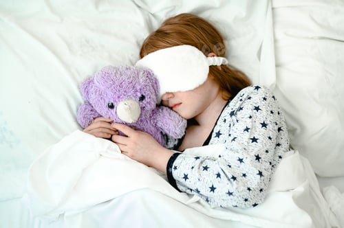 Preview: little girl with red hair sleeps on a bed with white sheets. she is wearing a sleep bandage