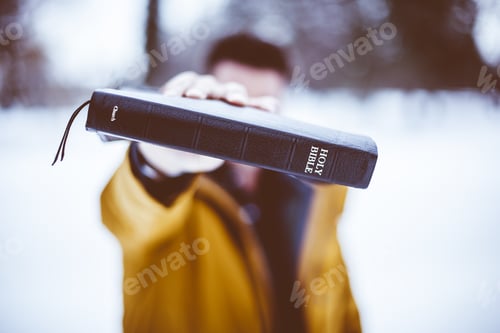 Preview: Closeup shot of a male holding up the bible towards the camera with a blurred background