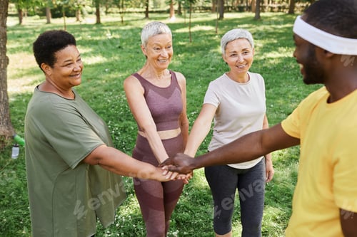 Preview: Active senior women stacking hands with trainer after enjoying outdoor workout
