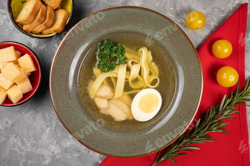 Preview: Bowl of steaming hot soup with pasta and an egg floating in the broth on a table