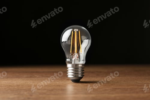 Preview: Vintage filament lamp bulb on wooden table against black background