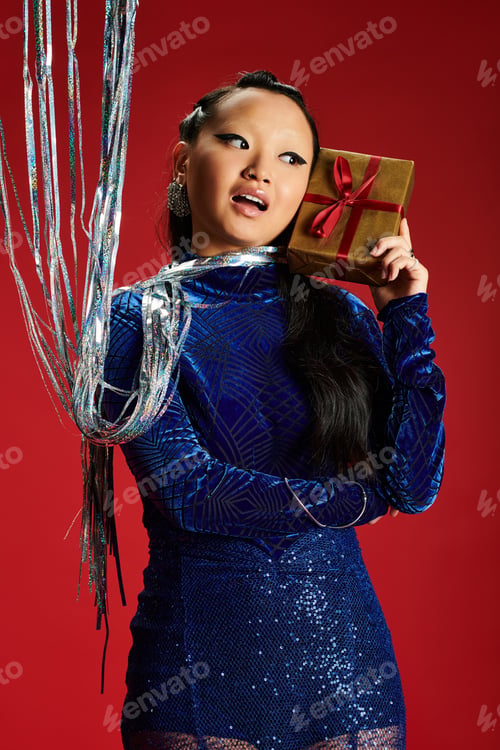 Preview: A stylish Asian woman celebrates with a shiny gift in a festive atmosphere during the holiday season