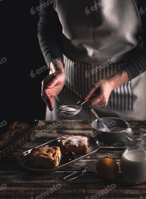 Preview: Close up of female chefs hands servicing slice of cake with cherries on dark background.