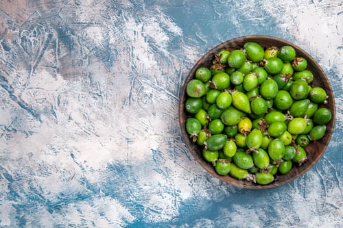 Preview: Close up view of delicious fresh feijoas in a brown pot on the left side of ice background