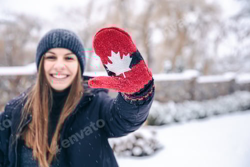 Preview: Happy young woman in red mittens with the flag of Canada in snowy weather.