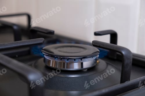 Preview: Burning gas burner with blue flames on kitchen black gas stove with a bokeh effect. gasoline
