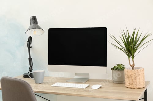 Preview: Workplace with computer, plants and lamp on wooden table. Empty black screen