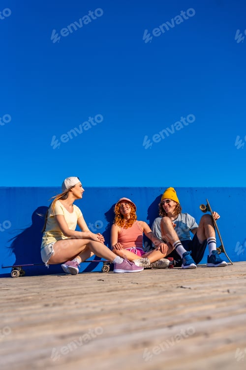 Preview: Group of young skaters relaxing against blue wall on sunny day