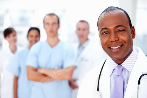 Preview: Confident doctor with medical team in background. Focus on doctor with colleagues in background.