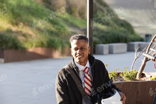 Preview: businessman with helmet and electric scooter resting outdoors