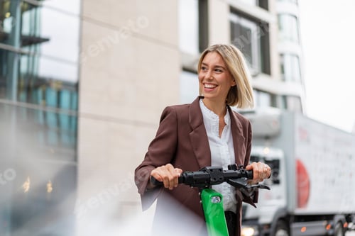 Preview: Happy young businesswoman with e-scooter in the city