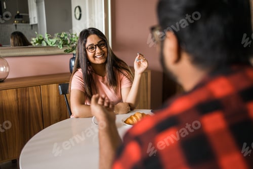 Preview: Happy couple eating breakfast and talking at dining table in morning. Indian girl and latino guy