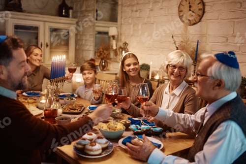Preview: Happy multigeneration Jewish family toasting at dining table while celebrating Hanukkah.