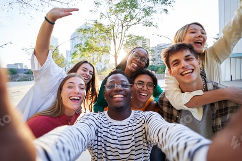 Preview: Cheerful multiethnic group of friends gathering outside using a phone to take a selfie together.