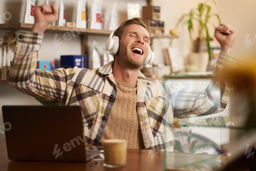 Preview: Portrait of excited, happy young man sitting behind the counter in cafe, working on laptop