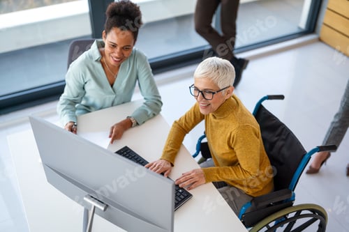 Preview: Disabled woman in wheelchair looking at computer, discussing startup project with interracial team
