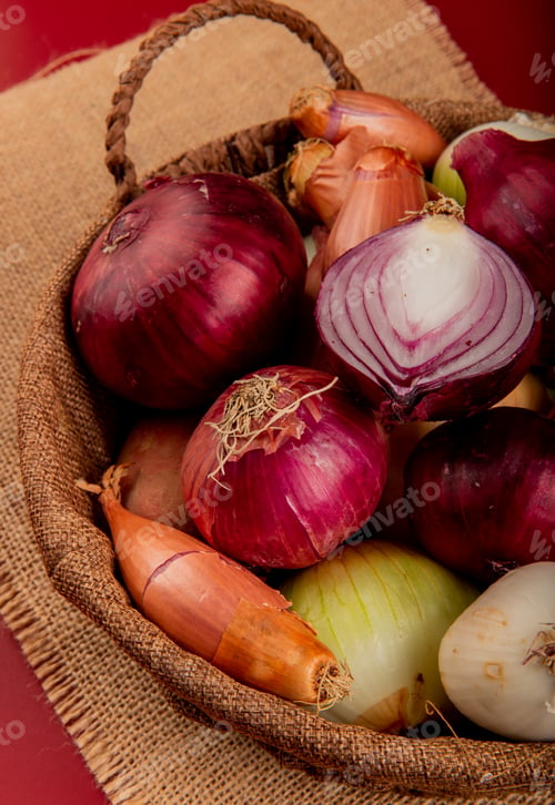 Preview: side view of different types of onion in basket on sackcloth on red background
