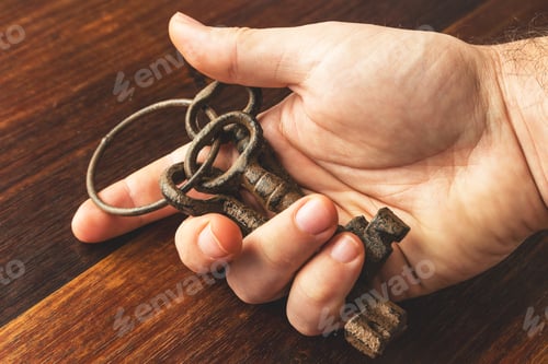 Preview: High angle shot of a person holding some old and rusted keys over a wooden surface