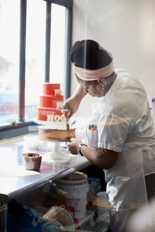 Preview: Young black woman frosting a cake at a bakery