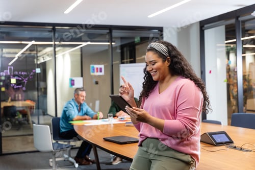 Preview: Smiling young biracial businesswoman using tablet pc while colleagues in background