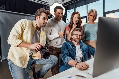 Preview: selective focus of happy creative director and assistants looking at computer monitor in photo