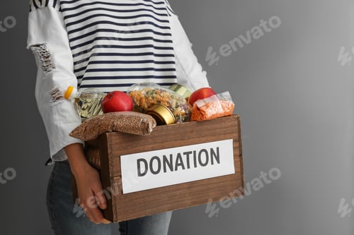Preview: Woman holding donation box with food on gray background, closeup