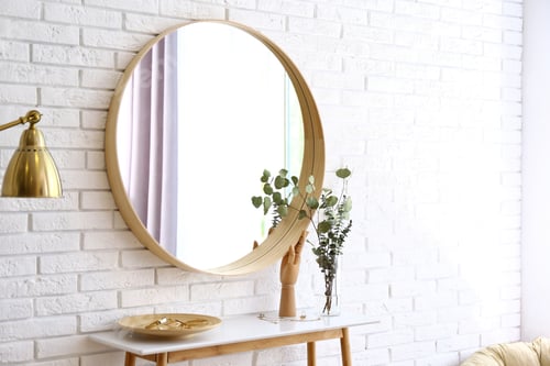 Preview: Big round mirror, table with jewelry and decor near brick wall in hallway interior