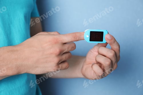 Preview: Young man checking pulse with blood pressure monitor on finger against color background, closeup