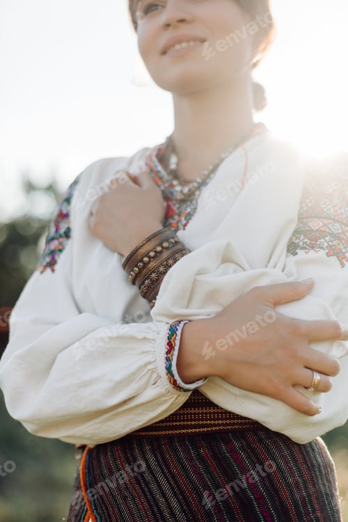 Preview: Young woman in traditional national embroidered shirt and skirt on nature at sunset.