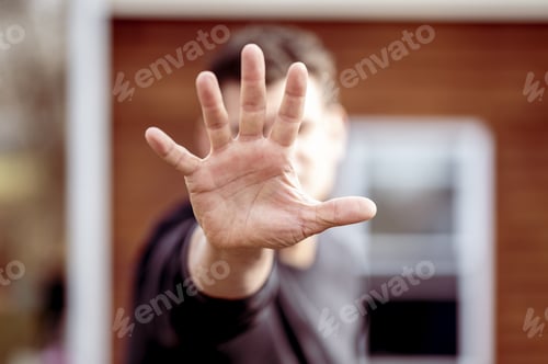 Preview: Shallow focus of a young Caucasian man doing the stop sign with his hand outdoors