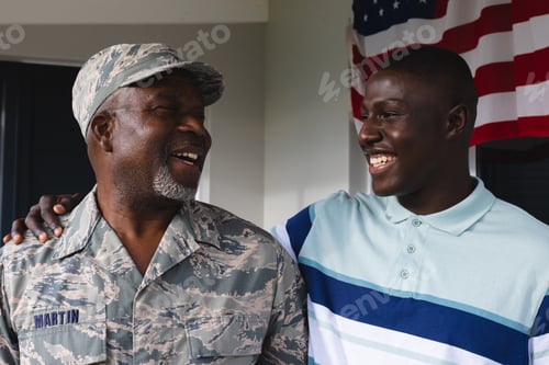 Preview: Happy african american military senior man looking at smiling mid adult son against house