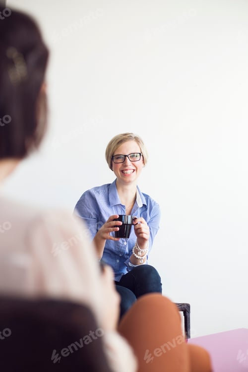 Preview: Happy businesswoman holding coffee mug while talking to colleague in office