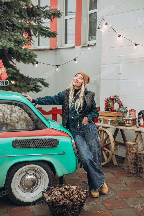 Preview: Young blonde woman near retro car with Christmas decorations