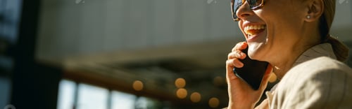 Preview: Side view of smiling female entrepreneur talking phone standing on modern office background