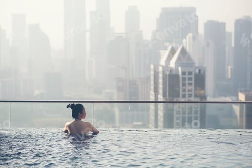 Preview: Young woman in outdoor swimming pool with city view at night