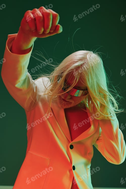 Preview: Fashionable individual with long blonde hair wearing a stylish white suit and colorful sunglasses