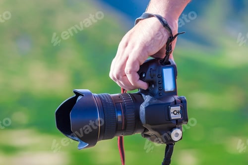 Preview: Hand of a man holding professional digital camera on blurred green background