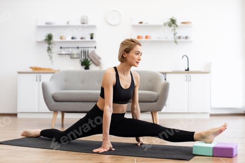 Preview: Woman practicing yoga splits at home on yoga mat