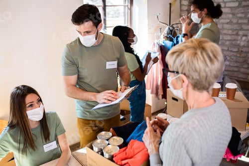 Preview: Group of volunteers with face mask working in community charity donation center.