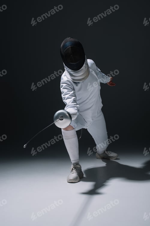 Preview: Fencer in fencing mask holding rapier while training on white surface on black background