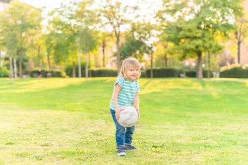 Vista previa: little boy standing on grass in park holding a ball
