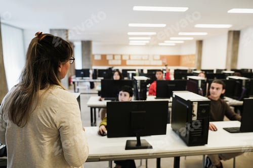 Preview: Mature teacher working with students inside computer room at school - Focus on woman shoulder