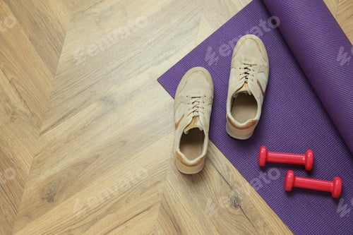 Preview: Dumbbells, sneakers and mat on wooden floor, above view. Space for text