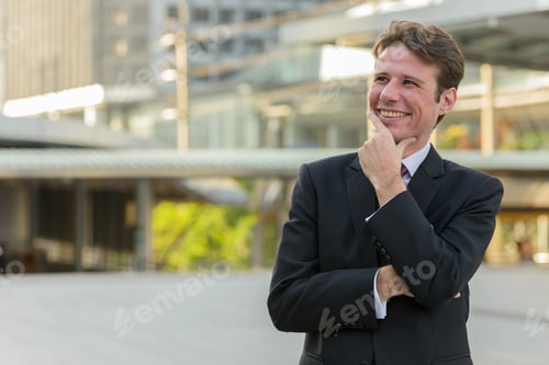 Preview: Happy businessman smiling and thinking in front of modern buildi