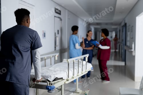 Preview: African american male doctor walking with hospital bed in corridor at hospital