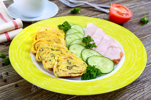 Preview: Omelette, egg roll with ham and fresh cucumber on a wooden table. Tasty healthy breakfast.
