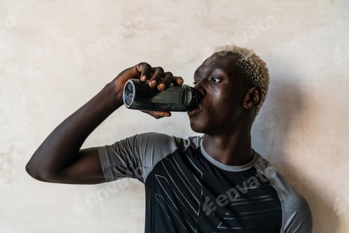 Preview: African american man drinking water while standing over wall indoors
