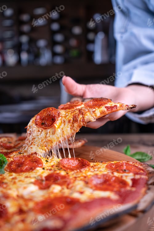 Preview: Vertical shot of a person getting a piece of delicious cheesy pepperoni pizza